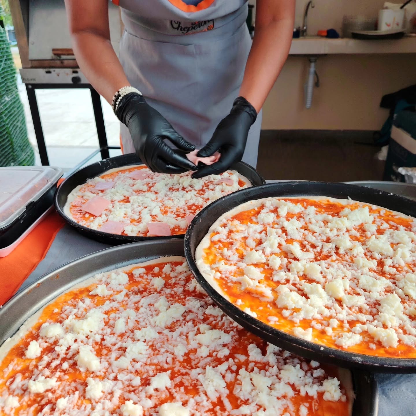 Manos con guantes terminando de armar una pizza, con el mandil de Cheperony